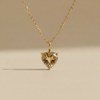 Gold necklace with a heart-shaped diamond pendant on a beige background