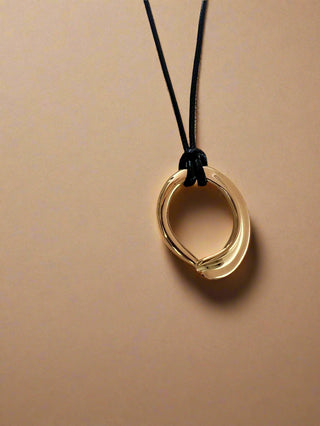 18k gold plated organic shaped round pendant on a cord black faux leather fabric displayed on a white pretty jewellery dish