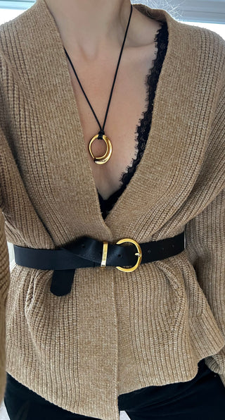 Organic gold pendant on black faux leather worn on model wearing a black lace brand, brown knitted cardigan with a black belt and black jeans