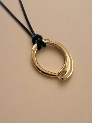 18k gold plated organic shaped pendant on a black faux leather cord necklace adjustable length displayed on a white jewellery dish
