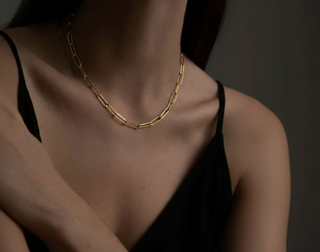 Gold chain necklace on a person wearing a black top against a dark background