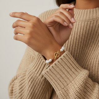 Person wearing a pearl bracelet on a beige sweater against a neutral background
