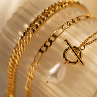 A gold-plated T-bar toggle necklace with a baroque pearl pendant on a light background.