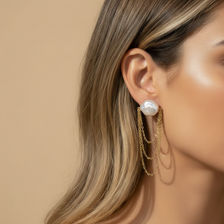 Close-up of a woman wearing pearl and gold earrings against a beige background