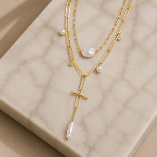 Gold necklace with pearl accents on a beige marble surface