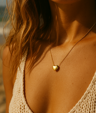 Close-up of a person wearing a gold heart-shaped necklace on a beach.