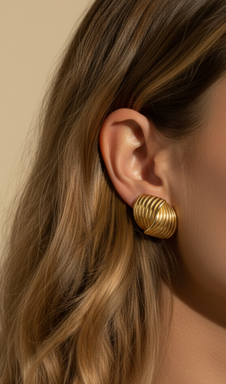 Gold hoop earrings worn by a person with wavy hair against a beige background