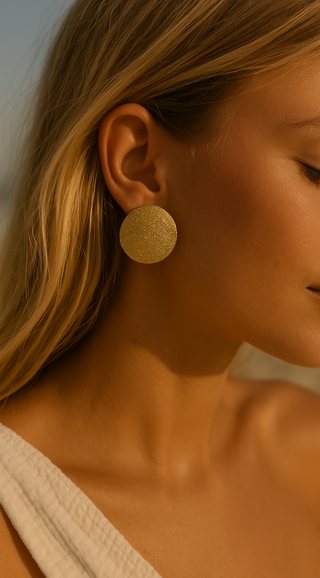 Close-up of a woman wearing large gold earrings. one shoulder top.