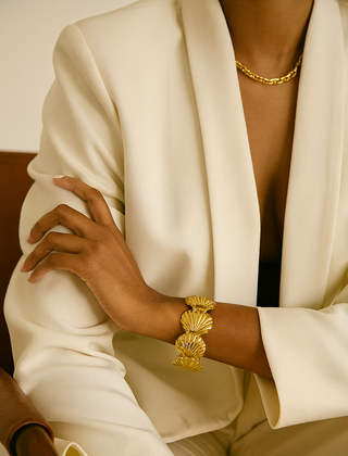 Person wearing a gold bracelet and gold necklace with a white outfit.