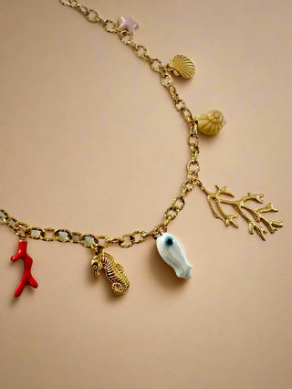 Gold necklace with various seashell charms on a light beige background