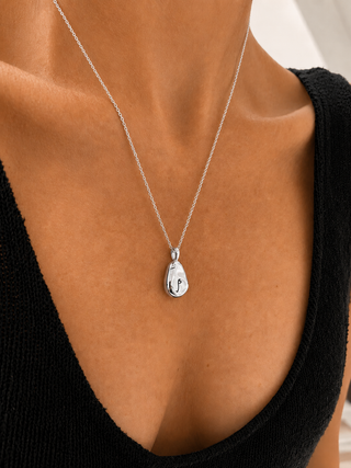 A gold pendant necklace with a small engraved anchor symbol, worn by a model in a black top.
