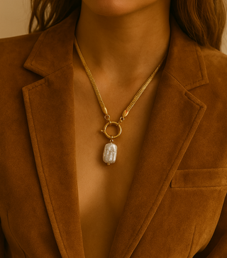 Person wearing a gold necklace with a pendant, dressed in a brown blazer.