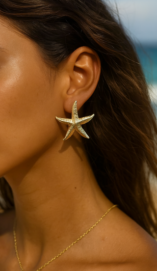 Woman wearing a gold starfish earring with a beach background
