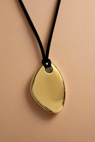 Gold pendant on a black cord against a white background