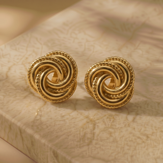 Pair of gold spiral earrings on a beige stone surface