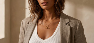 Woman wearing a beige blazer and white top with a necklace, standing against a neutral background