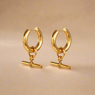 Pair of gold hoop earrings with small cylindrical charms on a white background