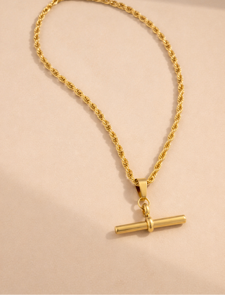 Gold necklace with a cylindrical pendant on a beige background