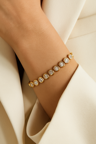 Gold bracelet with clear stones on a wrist against a white fabric background