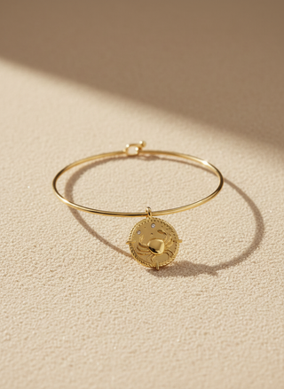 Gold bracelet with a round pendant on a beige background